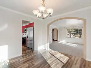 Unfurnished dining area featuring crown molding, a notable chandelier, and hardwood / wood-style flooring