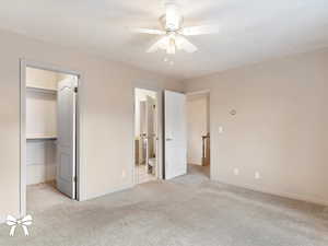 Unfurnished bedroom with ensuite bathroom, ceiling fan, light colored carpet, and a spacious closet