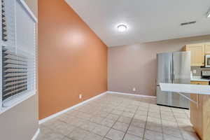 Kitchen with lofted ceiling, light tile patterned floors, a textured ceiling, range, and stainless steel refrigerator