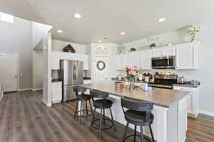 Kitchen featuring dark hardwood / wood-style flooring, a breakfast bar, stainless steel appliances, white cabinetry, and an island with sink