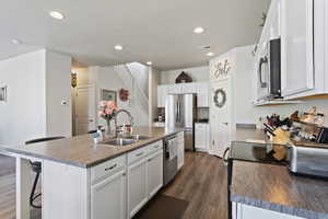 Kitchen featuring a center island with sink, sink, dark hardwood / wood-style floors, appliances with stainless steel finishes, and white cabinetry