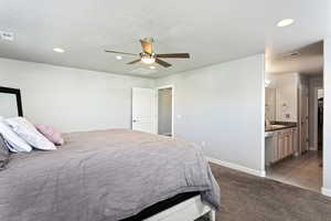 Bedroom featuring ceiling fan, sink, light carpet, and ensuite bath