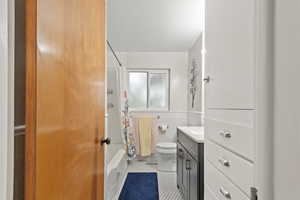 Full bathroom featuring vanity, shower / bath combo, tile patterned floors, toilet, and tile walls