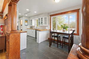 Kitchen with ornate columns, white cabinetry, stainless steel dishwasher, and wood counters