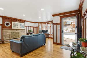 Living room featuring light wood-type flooring, a stone fireplace, and ornamental molding