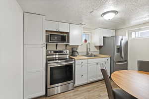 Kitchen featuring wooden counters, stainless steel appliances, sink, light hardwood / wood-style flooring, and white cabinets