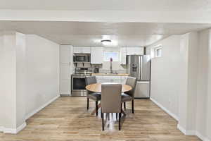 Kitchen with sink, light wood-type flooring, a textured ceiling, appliances with stainless steel finishes, and white cabinetry