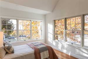 Bedroom with vaulted ceiling,, and multiple windows and wood floors.