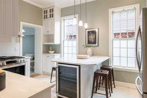 Kitchen featuring white cabinetry, wine cooler, pendant lighting, a kitchen bar, and appliances with stainless steel finishes