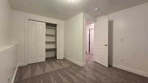 Unfurnished bedroom featuring dark colored carpet, a textured ceiling, and a closet