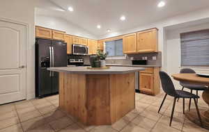 Kitchen featuring black refrigerator with ice dispenser, range with electric stovetop, lofted ceiling, light brown cabinetry, and a kitchen island