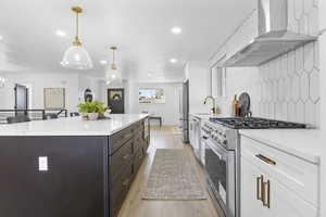 Kitchen with white cabinetry, wall chimney exhaust hood, pendant lighting, high quality appliances, and light wood-type flooring