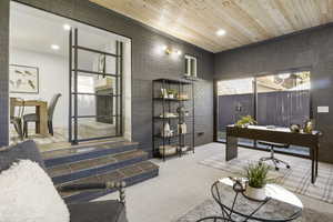 Carpeted home office featuring crown molding, wood ceiling, and brick wall