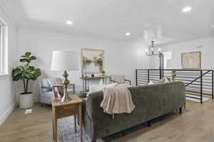 Living room with light wood-type flooring, ornamental molding, and a notable chandelier