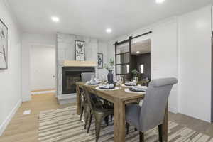 Dining room with light wood-type flooring, a barn door, a large fireplace, and crown molding