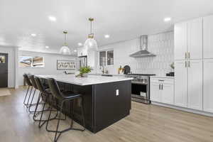 Kitchen featuring wall chimney range hood, light hardwood / wood-style flooring, pendant lighting, high quality appliances, and white cabinets