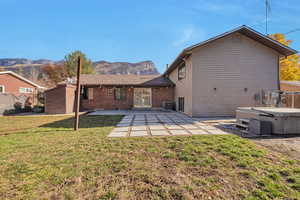 Back of house featuring a mountain view, a patio, a hot tub, and a lawn