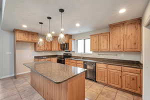 Kitchen with a center island, sink, stainless steel appliances, decorative light fixtures, and light tile patterned flooring