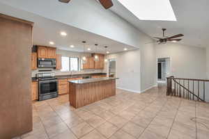 Kitchen with sink, stainless steel appliances, lofted ceiling with skylight, decorative light fixtures, and a kitchen island