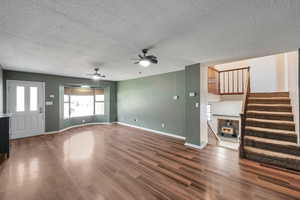 Unfurnished living room with a wood stove, ceiling fan, dark wood-type flooring, and a textured ceiling