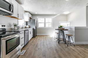 Kitchen with white cabinetry, sink, stainless steel appliances, light hardwood / wood-style floors, and a breakfast bar