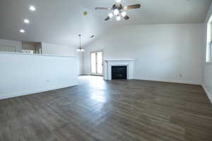 Unfurnished living room featuring ceiling fan with notable chandelier, tile flooring, and vaulted ceiling