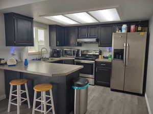 UpdatedK kitchen featuring sink, a breakfast bar area, light wood-type flooring, kitchen peninsula, and stainless steel appliances LVP floor