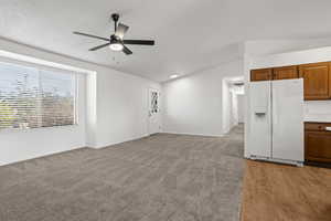 Unfurnished living room with ceiling fan, light carpet, and vaulted ceiling