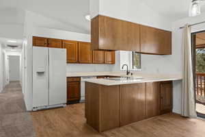 Kitchen featuring vaulted ceiling, kitchen peninsula, a healthy amount of sunlight, and white appliances