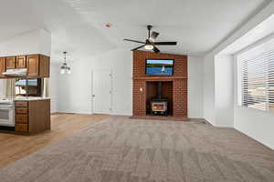 Unfurnished living room with lofted ceiling, light hardwood / wood-style floors, a wood stove, and ceiling fan