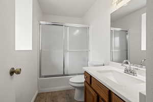 Full bathroom featuring shower / bath combination with glass door, toilet, vanity, and hardwood / wood-style flooring