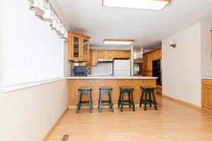 Kitchen with kitchen peninsula, light hardwood / wood-style floors, a breakfast bar, black microwave, and white fridge