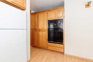 Kitchen with light hardwood / wood-style flooring, black appliances, and a textured ceiling