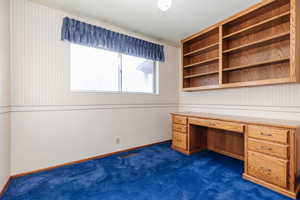 Unfurnished office featuring dark colored carpet and built in desk