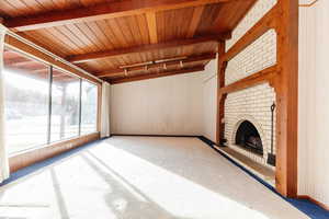 Unfurnished living room with beam ceiling, rail lighting, a brick fireplace, and wood ceiling