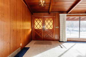 Interior space with beam ceiling, an inviting chandelier, wooden ceiling, and wood walls