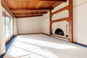 Unfurnished living room with a fireplace, rail lighting, wooden ceiling, and beamed ceiling