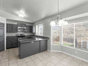 Kitchen with sink, hanging light fixtures, vaulted ceiling, appliances with stainless steel finishes, and a chandelier