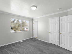 Unfurnished bedroom featuring a textured ceiling, dark carpet, and ornamental molding