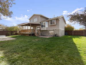 Back of property with a lawn, a wooden deck, and central AC