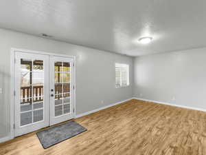 Empty room featuring french doors, a healthy amount of sunlight, a textured ceiling, and light wood-type flooring