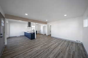 Kitchen with kitchen peninsula, wall chimney range hood, dark wood-type flooring, and a breakfast bar area