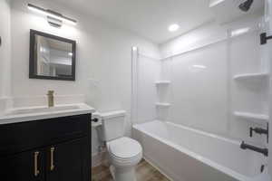 Full bathroom with hardwood / wood-style floors, vanity, shower / bath combination, and toilet