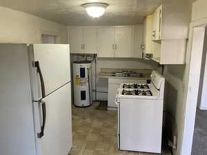 Kitchen with white appliances, electric water heater, and white cabinetry