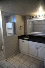 Bathroom with tile patterned flooring, vanity, toilet, and a textured ceiling