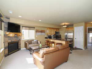 Carpeted living room featuring a stone fireplace and plenty of natural light