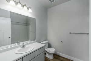 Bathroom with wood-type flooring, toilet, vanity, and a shower