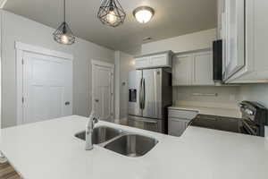 Kitchen with a textured ceiling, sink, gray cabinetry, appliances with stainless steel finishes, and decorative light fixtures