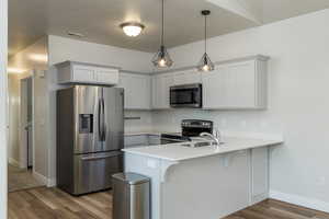 Kitchen with kitchen peninsula, white cabinetry, pendant lighting, and appliances with stainless steel finishes