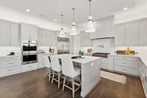 Kitchen with appliances with stainless steel finishes, backsplash, dark hardwood / wood-style floors, and a kitchen island